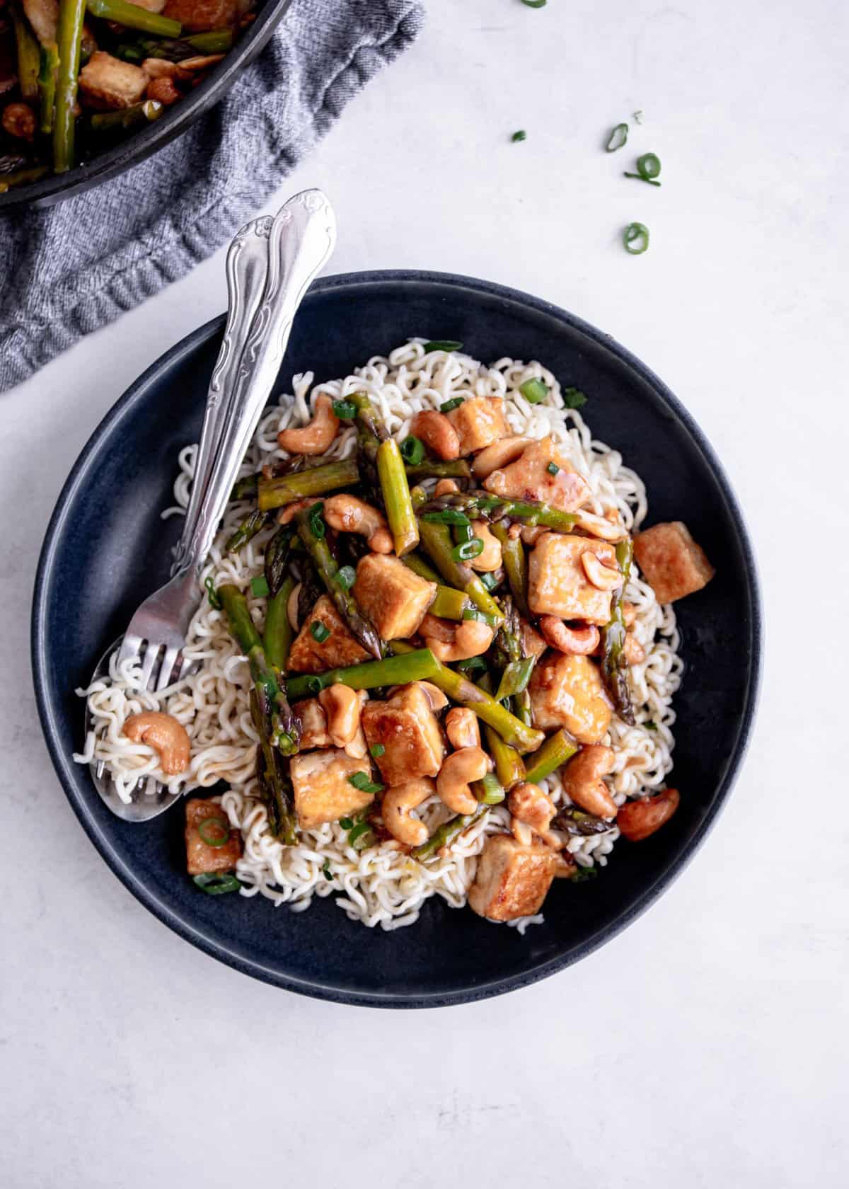 overhead image of tofu and vegetable stir fry over noodles in a black bowl