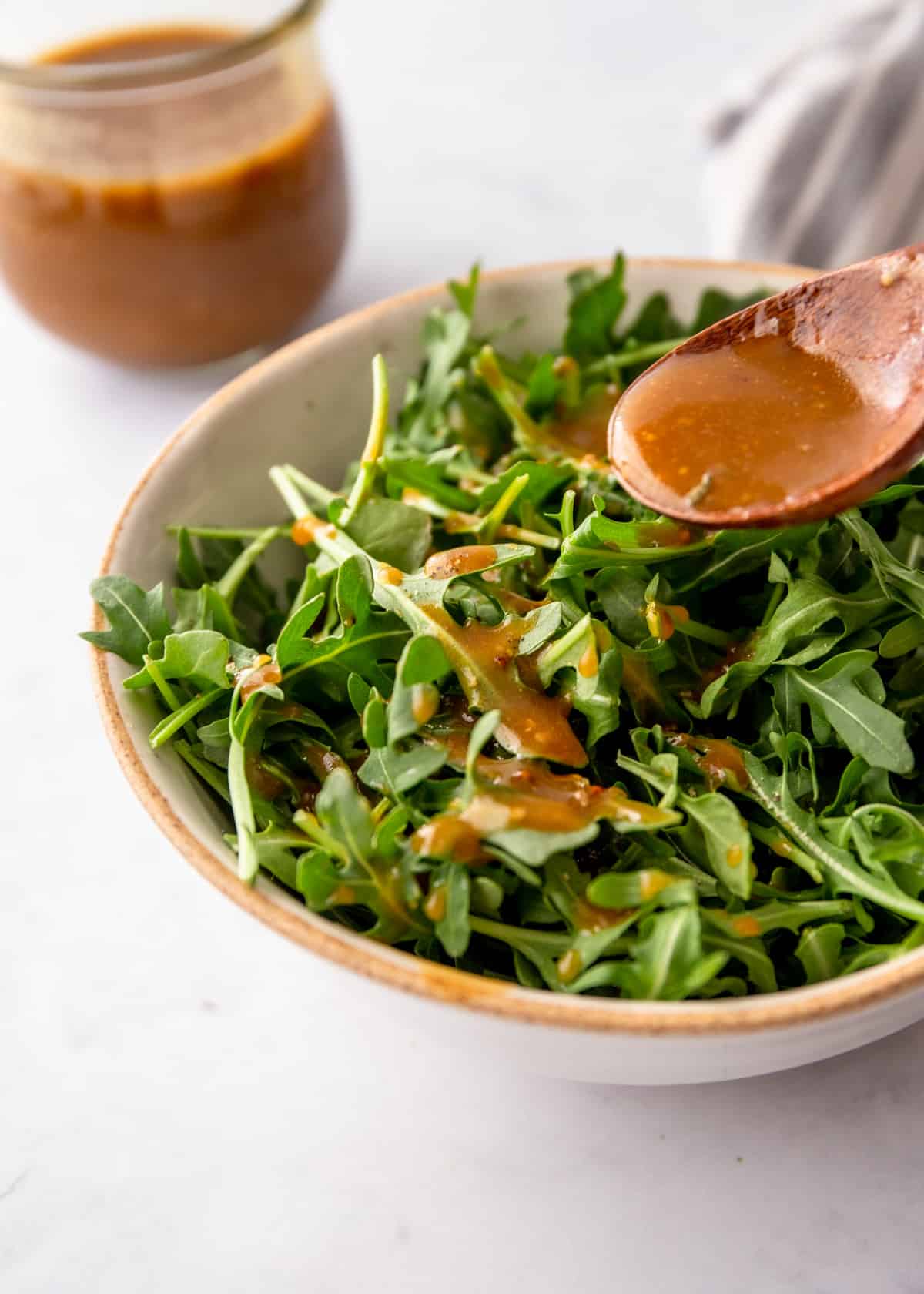 spooning vinaigrette over a salad in a white bowl
