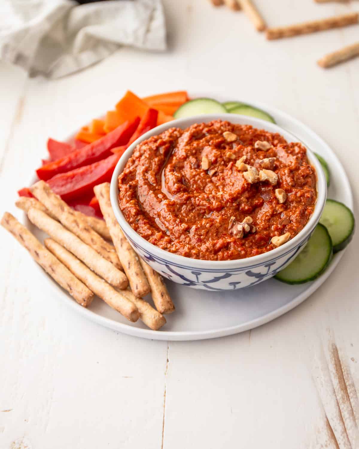red pepper dip in a bowl with vegetables on a white plate