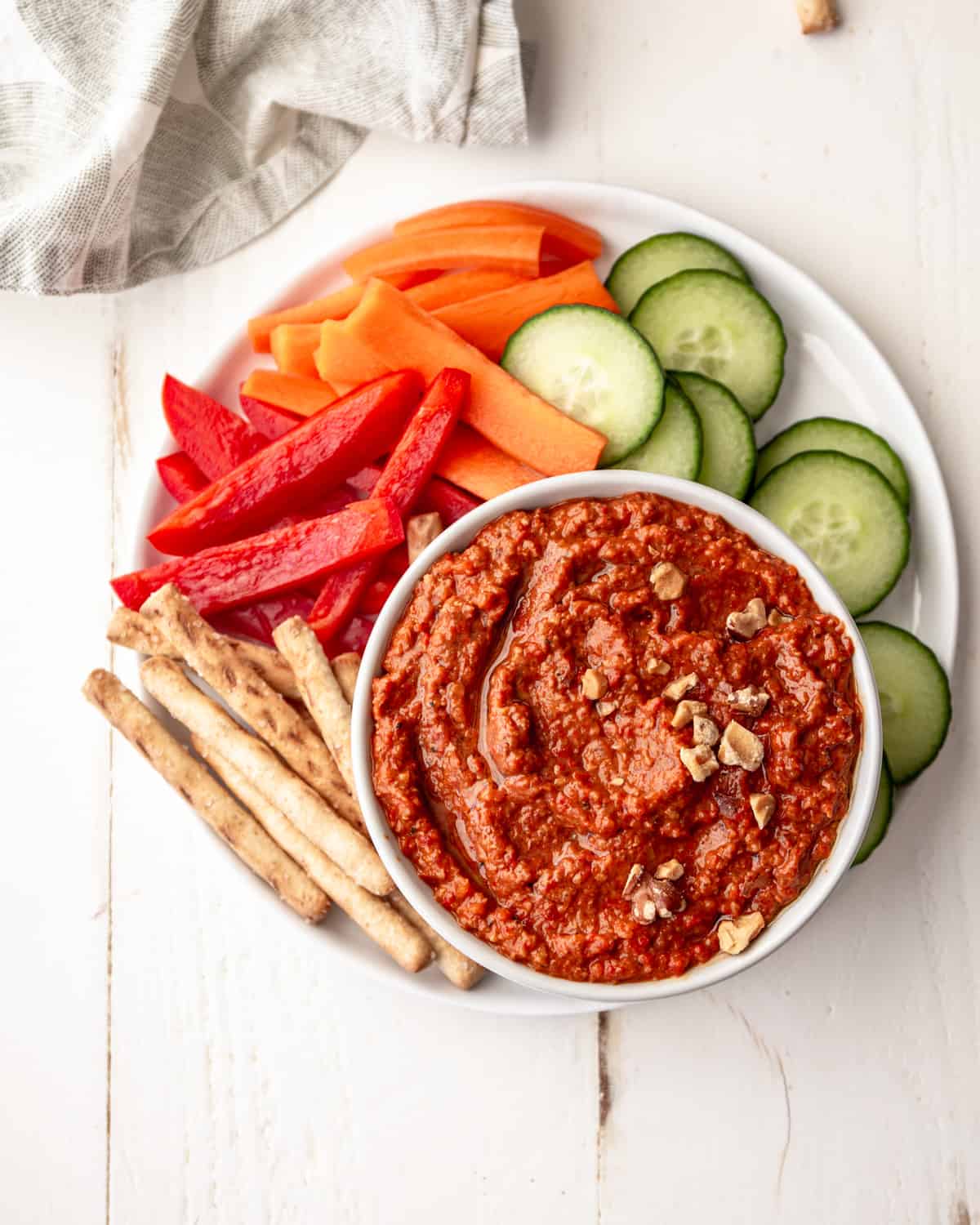 red pepper dip in a bowl with vegetables on a white plate