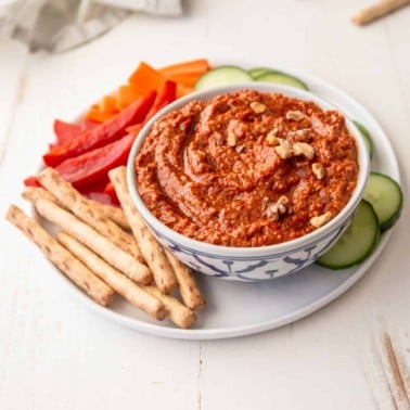 muhammara in a bowl on a white plate with vegetables