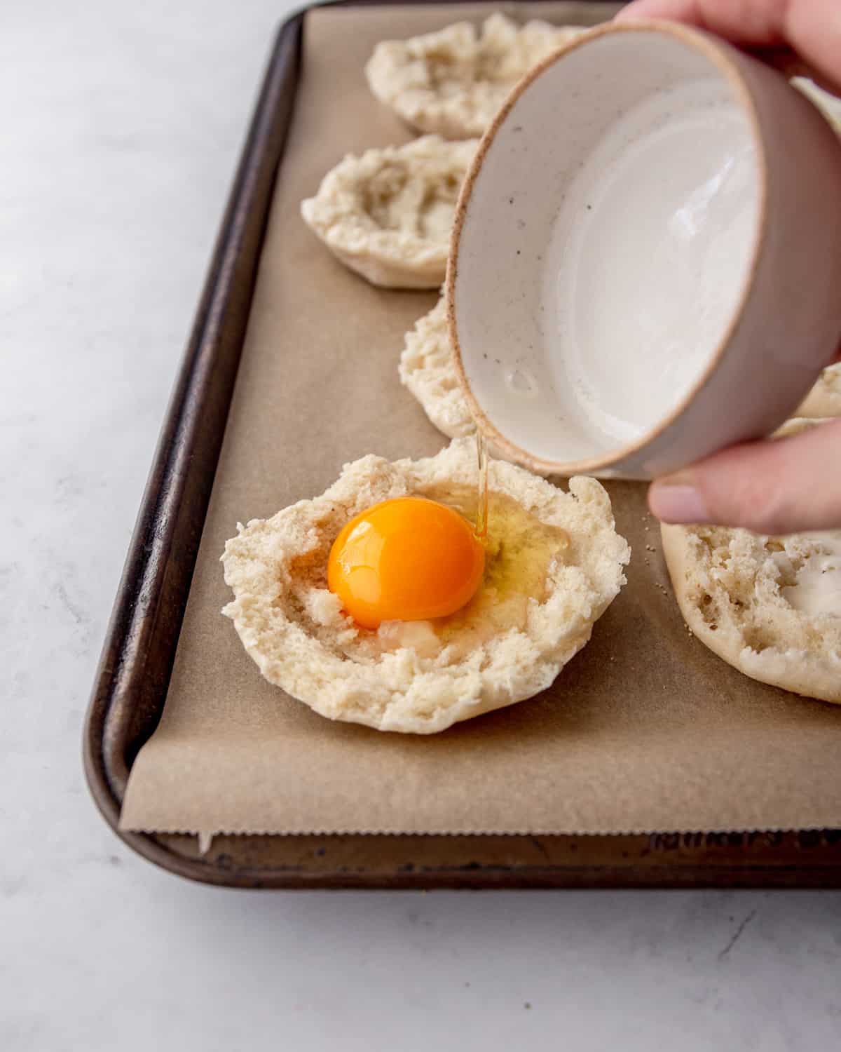 adding raw egg to center of english muffins on a parchment lined sheet pan