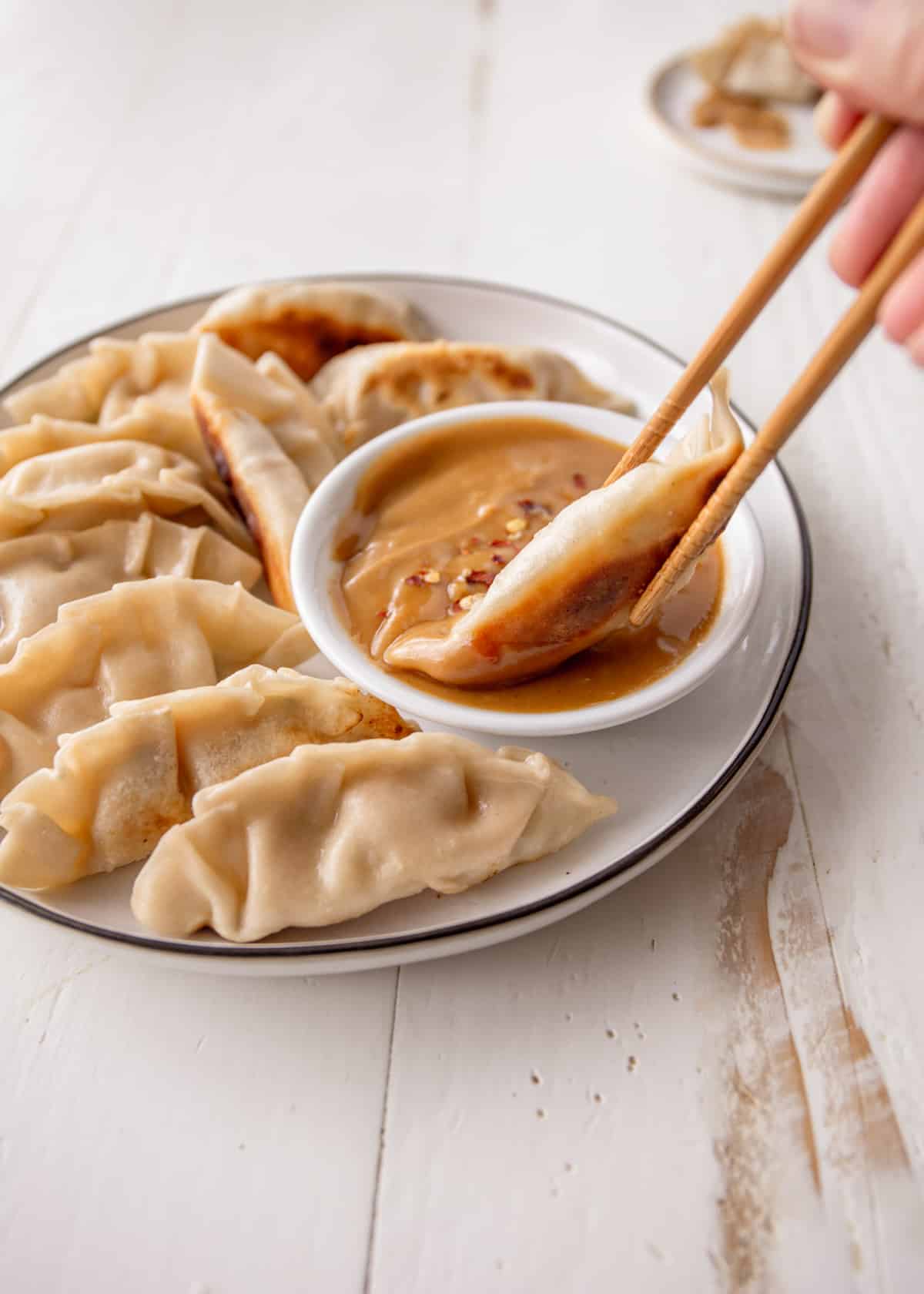 dipping a potsticker into a small bowl of peanut sauce