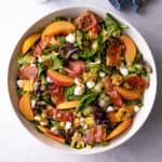 overhead photo of summer salad with corn, peaches and prosciutto in a white bowl