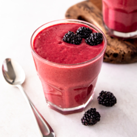 a blackberry smoothie in a glass on a white countertop with a spoon