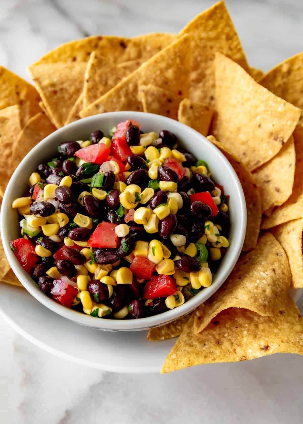 salsa in a small white bowl on a white plate with corn tortilla chips