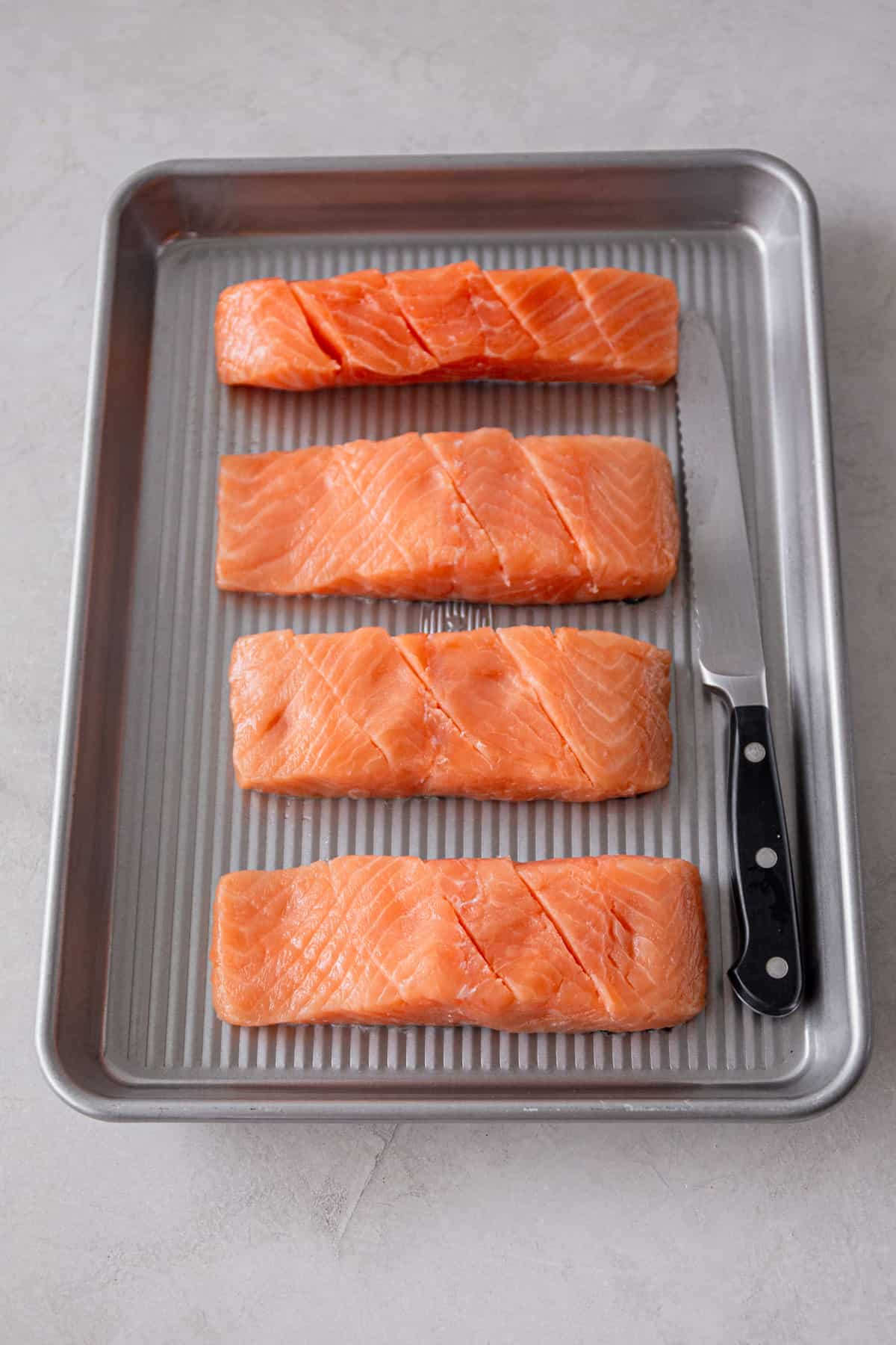 overhead image of scored salmon fillets on a metal sheet pan