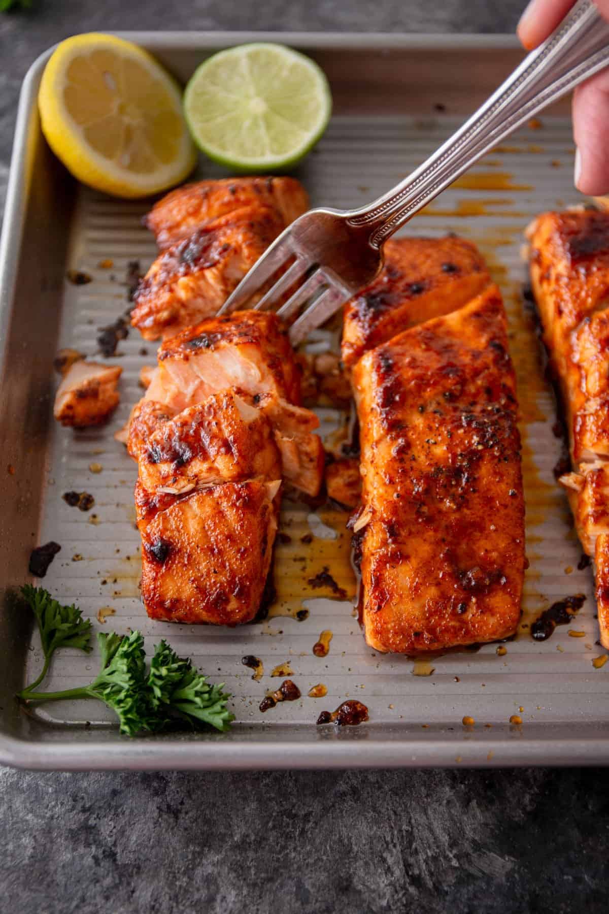 flaking broiled salmon with a fork on a metal sheet pan