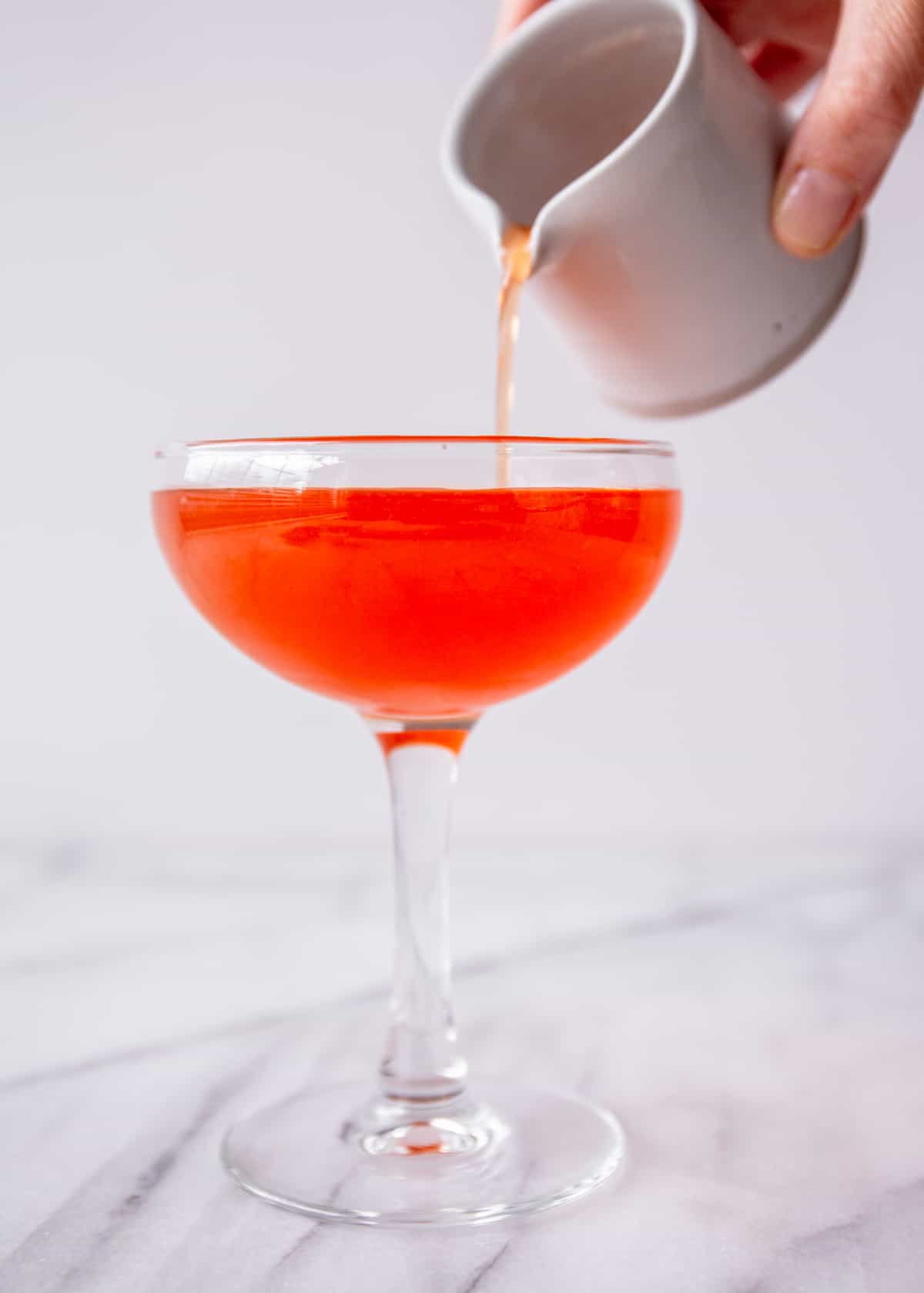 pouring an orange paper plane cocktail into a glass