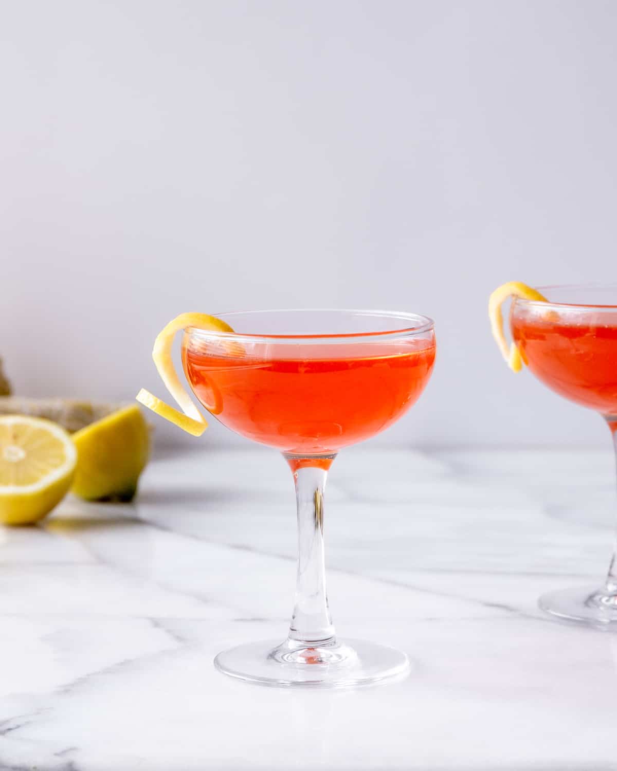 a bright orange cocktail in a glass with a twist of lemon on the rim