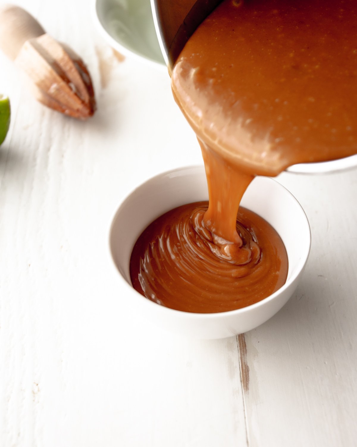 overhead image of pouring peanut sauce into a small white bowl