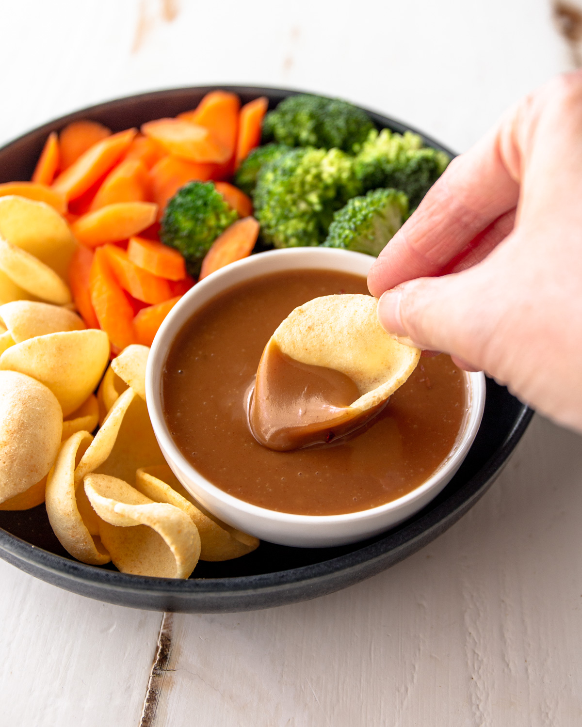 dipping a chip into peanut sauce in a white bowl