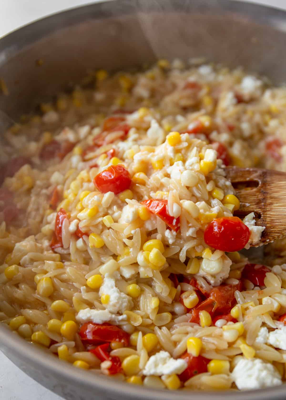 stirring one pot pasta with feta, tomatoes and corn in a skillet