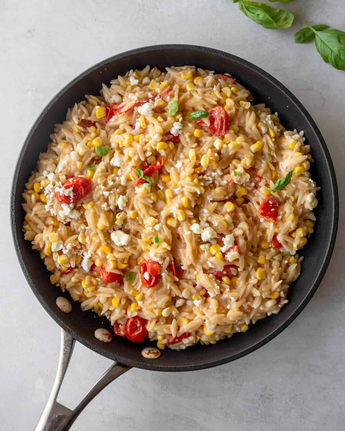 One-Pot Orzo com tomate, milho e queijo Feta em uma frigideira sobre uma bancada cinza