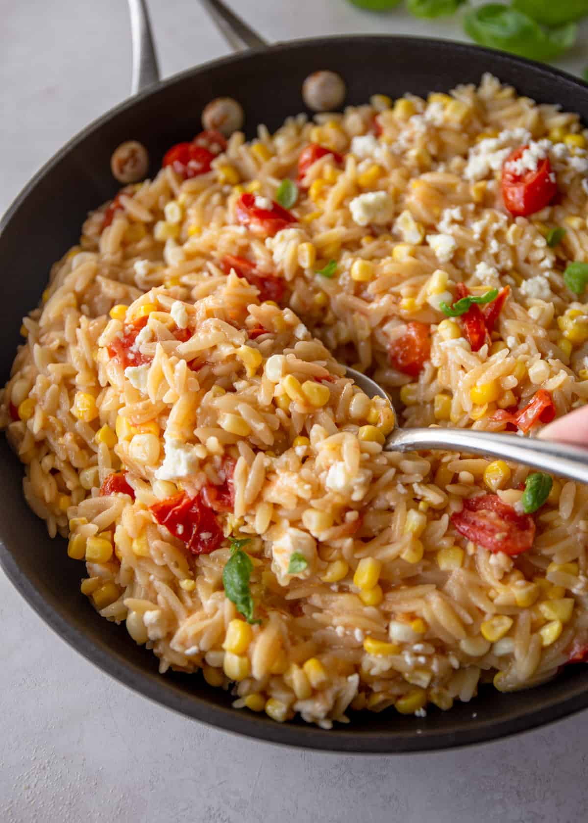 a spoon in a skillet of one pot pasta with tomatoes, corn and feta