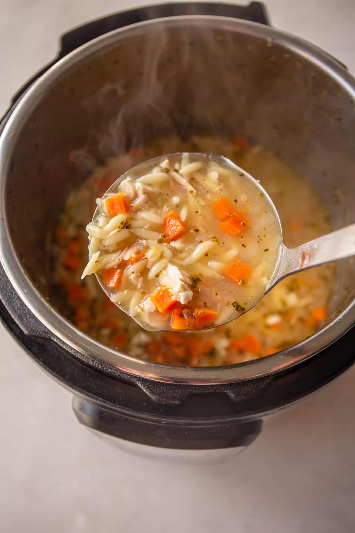 a ladle of chicken orzo soup over an instant pot