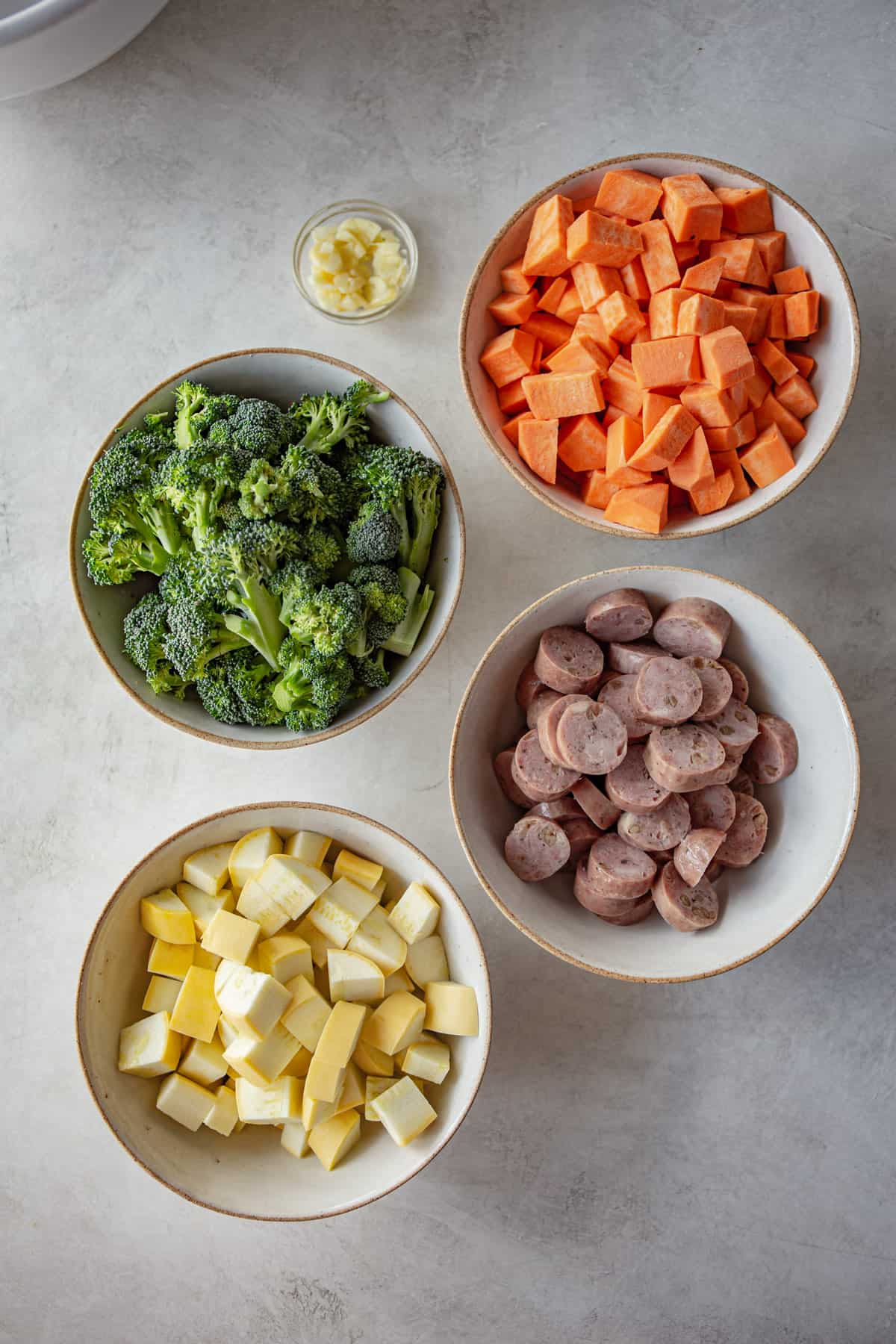 overhead image of ingredients for sheet pan meal in small white bowls on a grey countertop