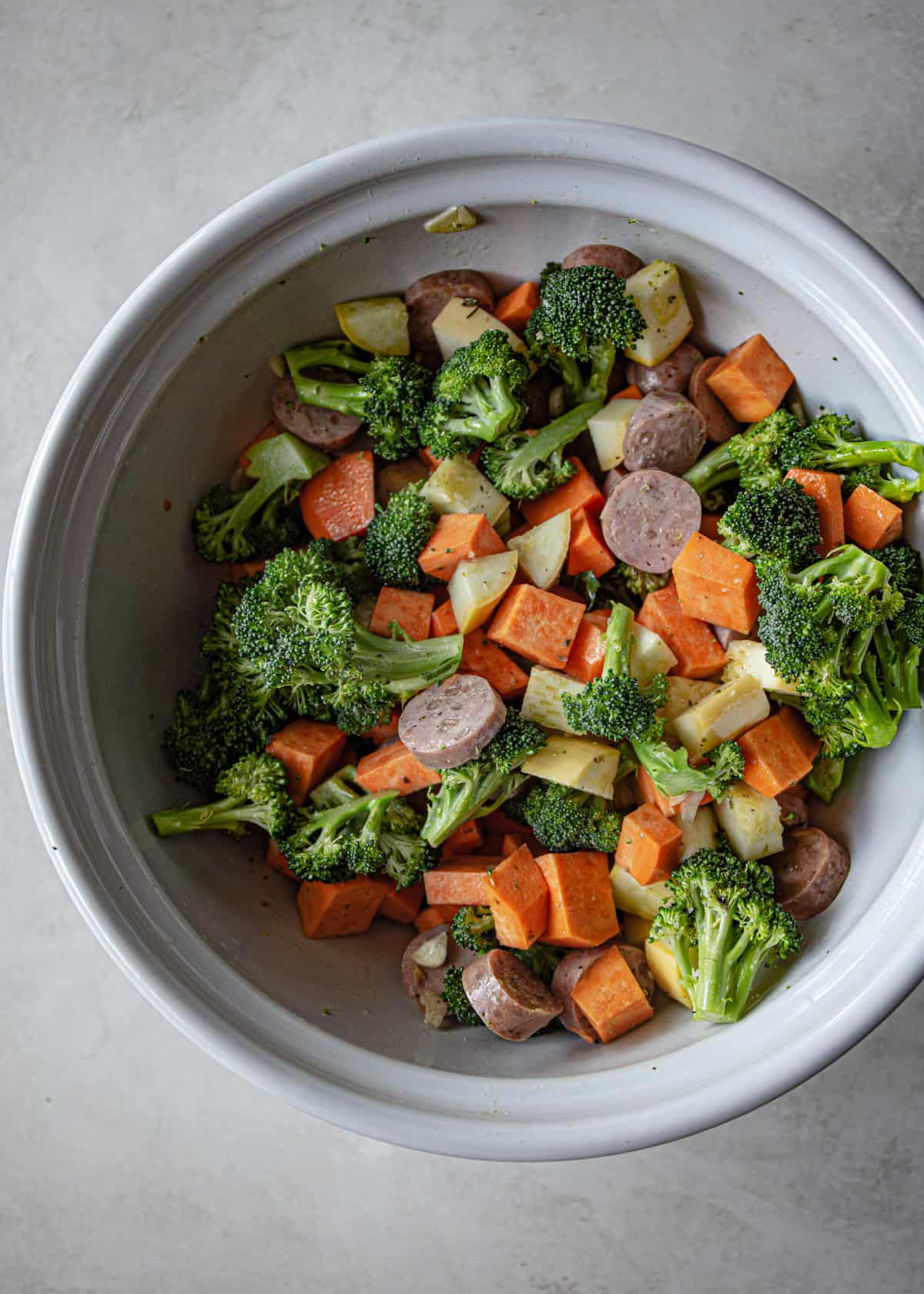 overhead image of sausage and raw vegetables in a white bowl