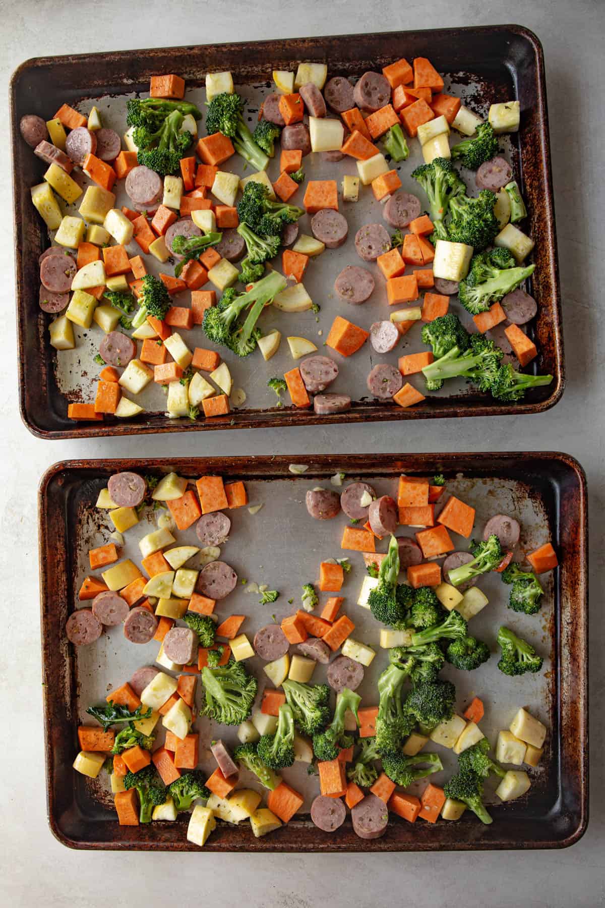 overhead image of raw vegetables and sausage slices on two sheet pans