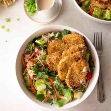 crispy chicken strips on top of a salad in a white bowl