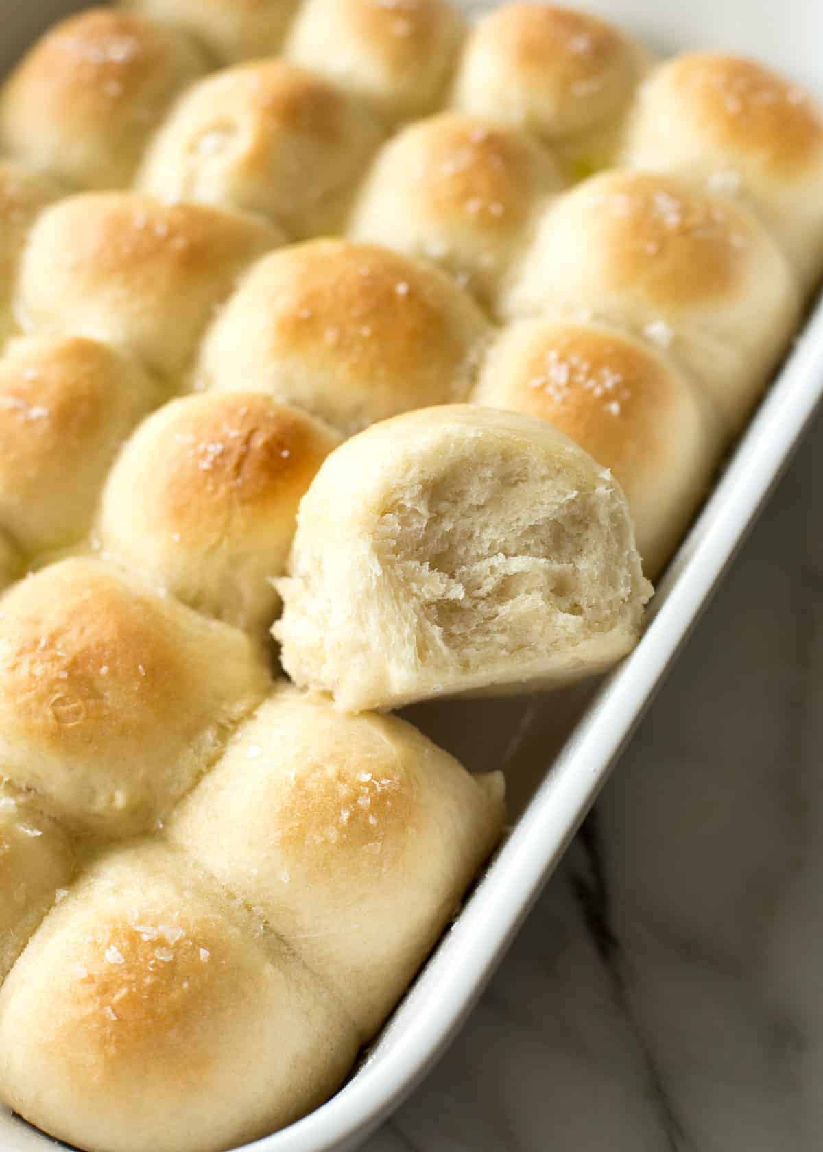 pulling a roll out of a white baking dish full of rolls