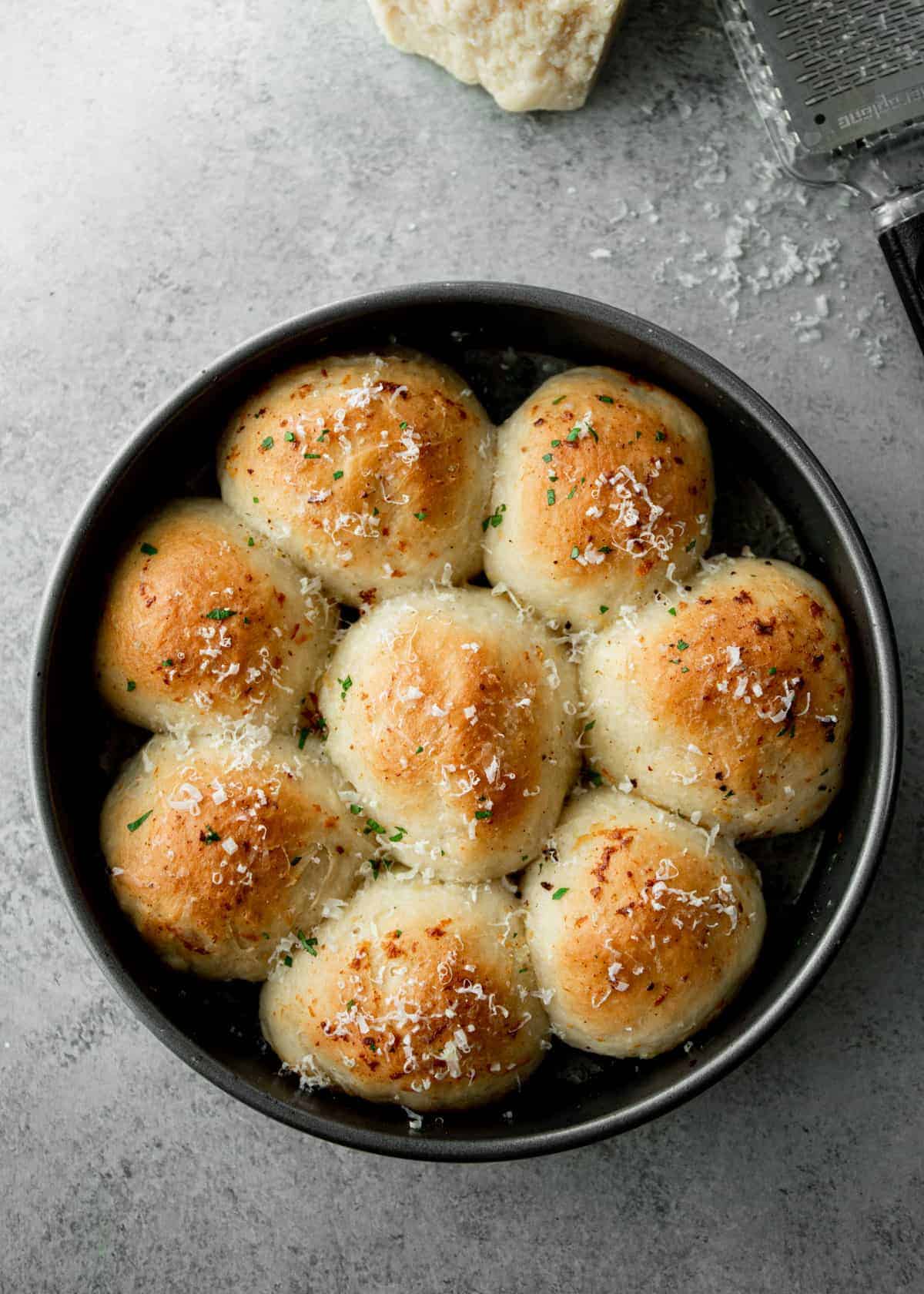 overhead view of garlic dinner rolls in a round pan on a grey countertop