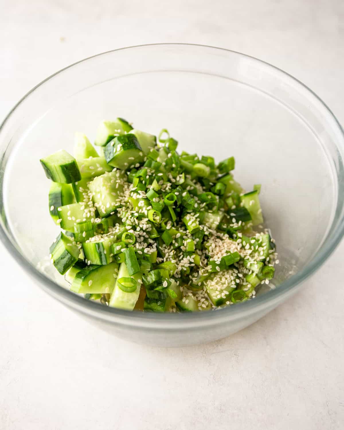 cucumbers, green onions and sesame seeds in a clear glass bowl