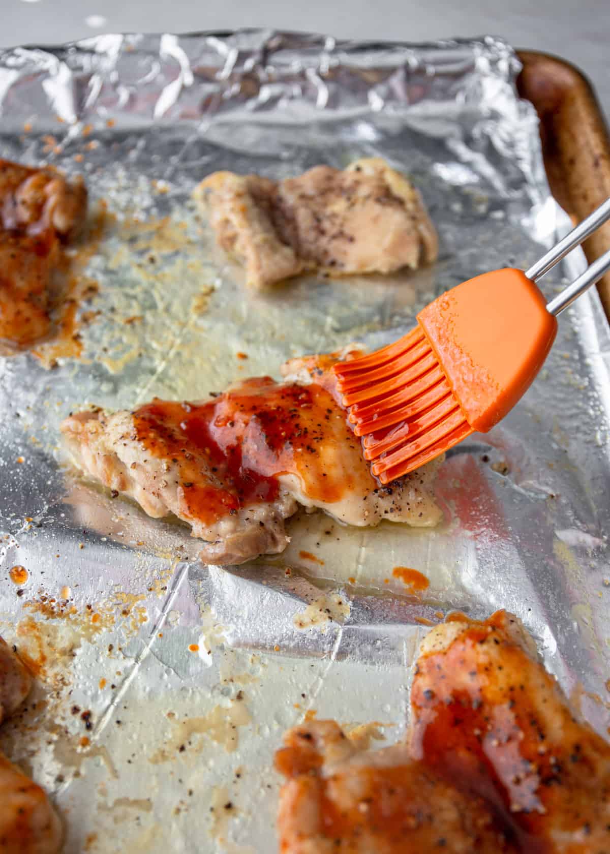 brushing spicy glaze on chicken pieces on a foil lined sheet pan
