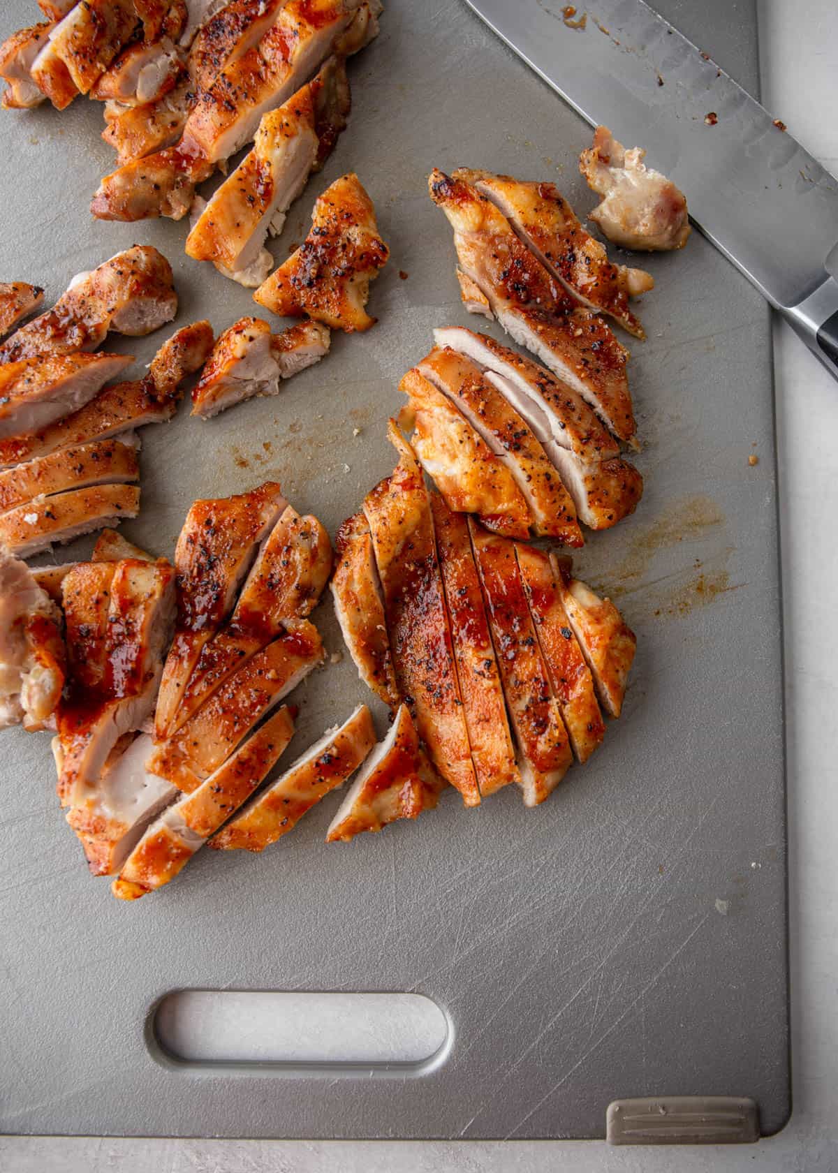 sliced cooked chicken on a grey cutting board