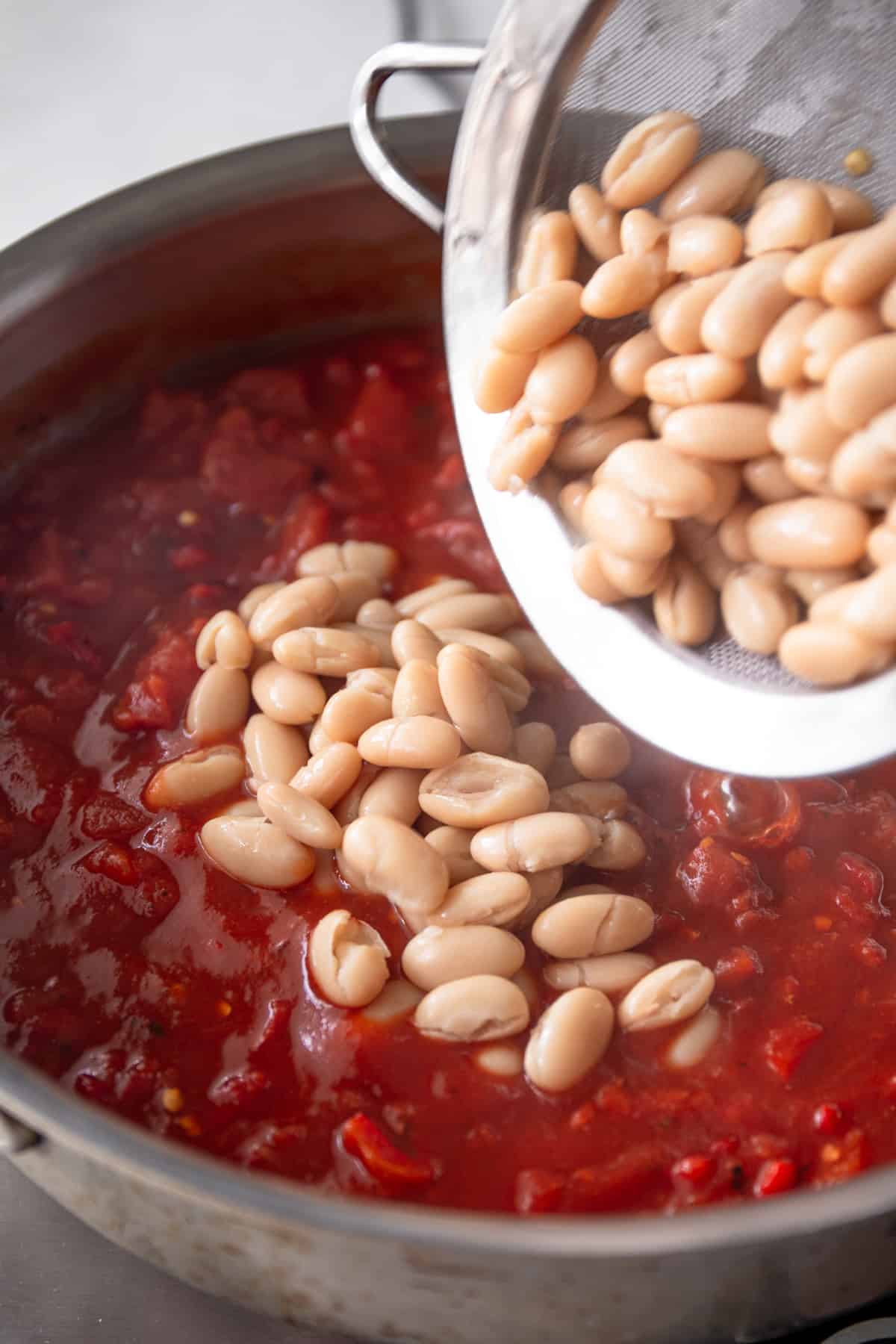 adding white beans to tomato sauce in a large skillet