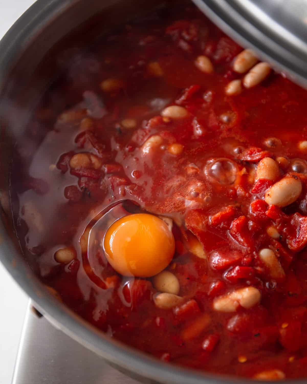 adding an egg to tomato sauce in a dutch oven