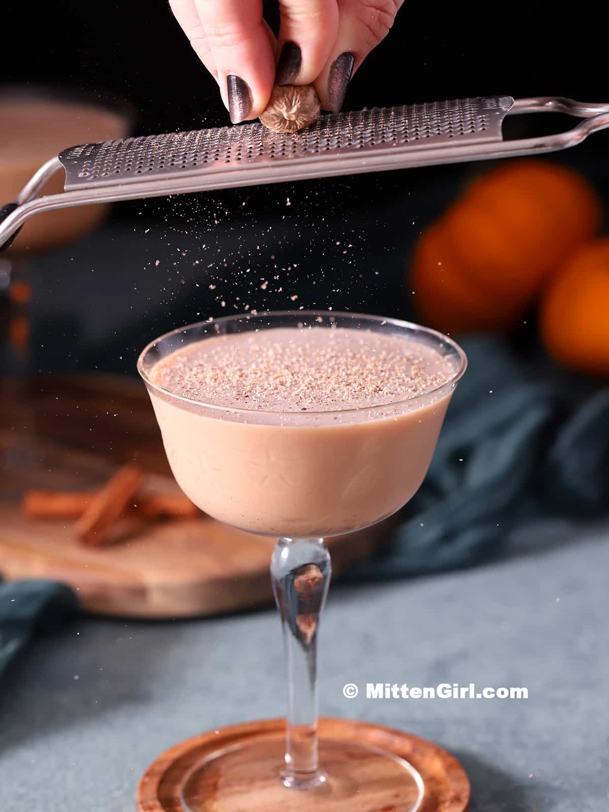 sprinkling nutmeg over martini on a grey countertop