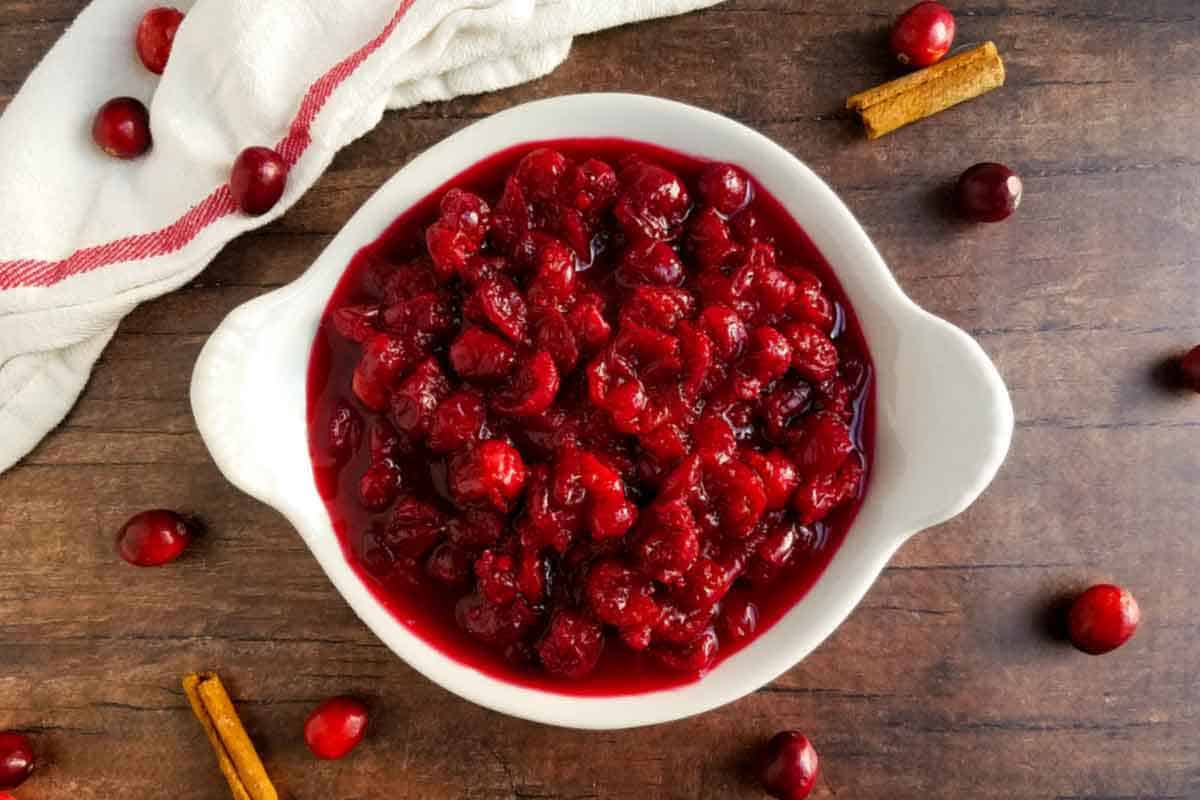 an overhead view of roasted cranberries in a white bowl on a wooden table