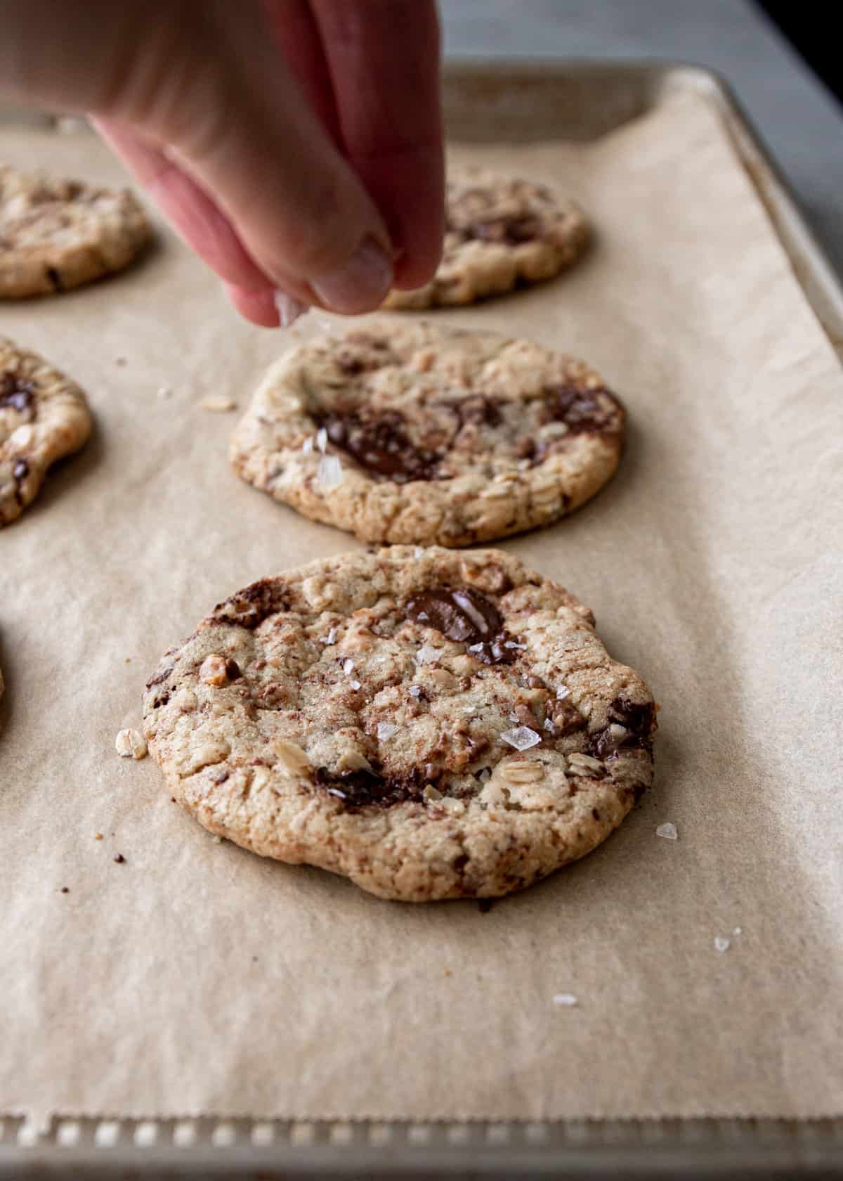 sprinkling salt flakes on top of baked cookies on a parchment lined sheet pan