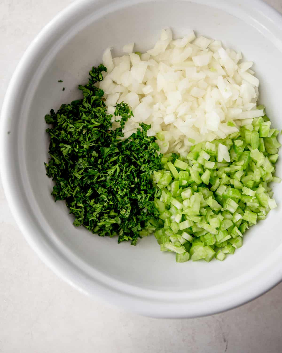onion, celery and herbs in a large white mixing bowl