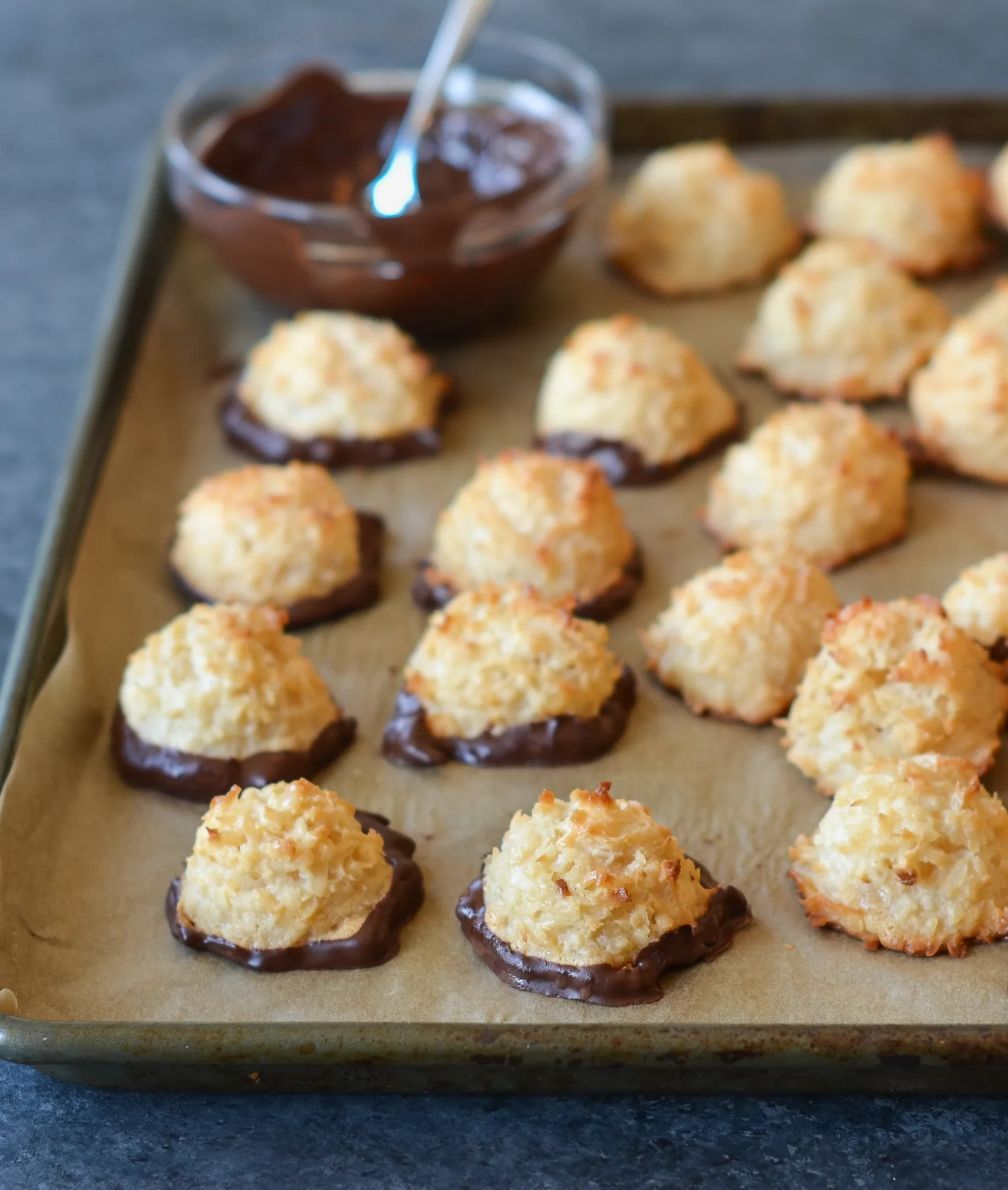 chocolate dipped coconut macarons on a parchment lined sheet pan