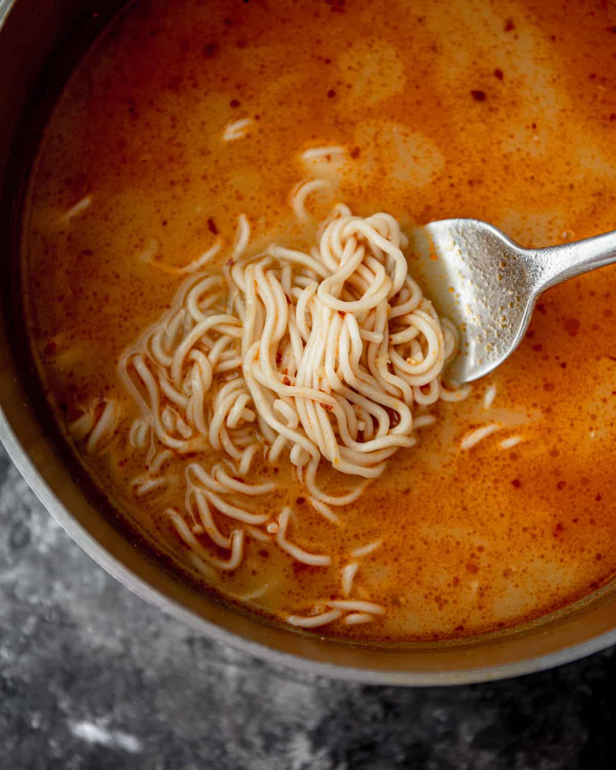 a fork holding ramen noodles in a broth