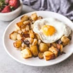 a white plate of crispy home fries with a fried egg on top