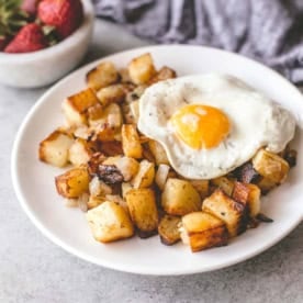 a white plate of crispy home fries with a fried egg on top