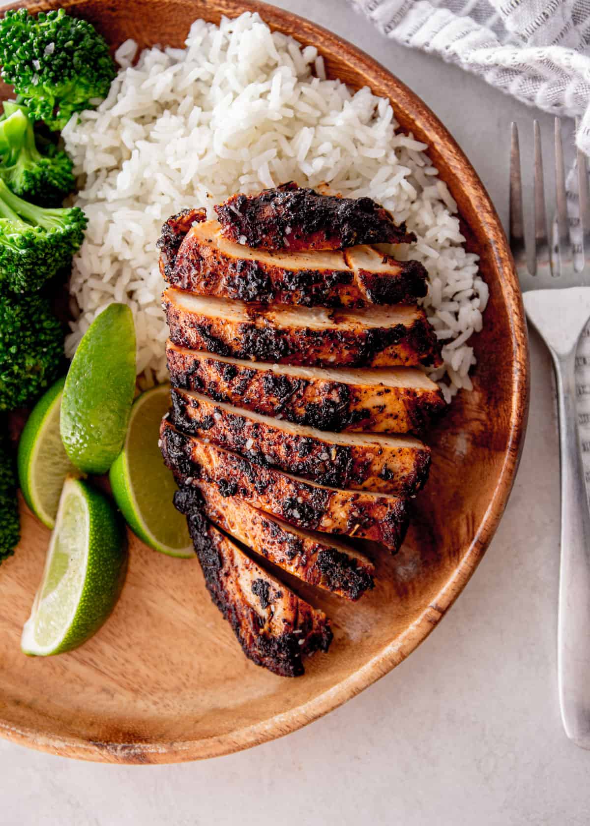 sliced blackened chicken on a round wooden plate with rice and lime slices