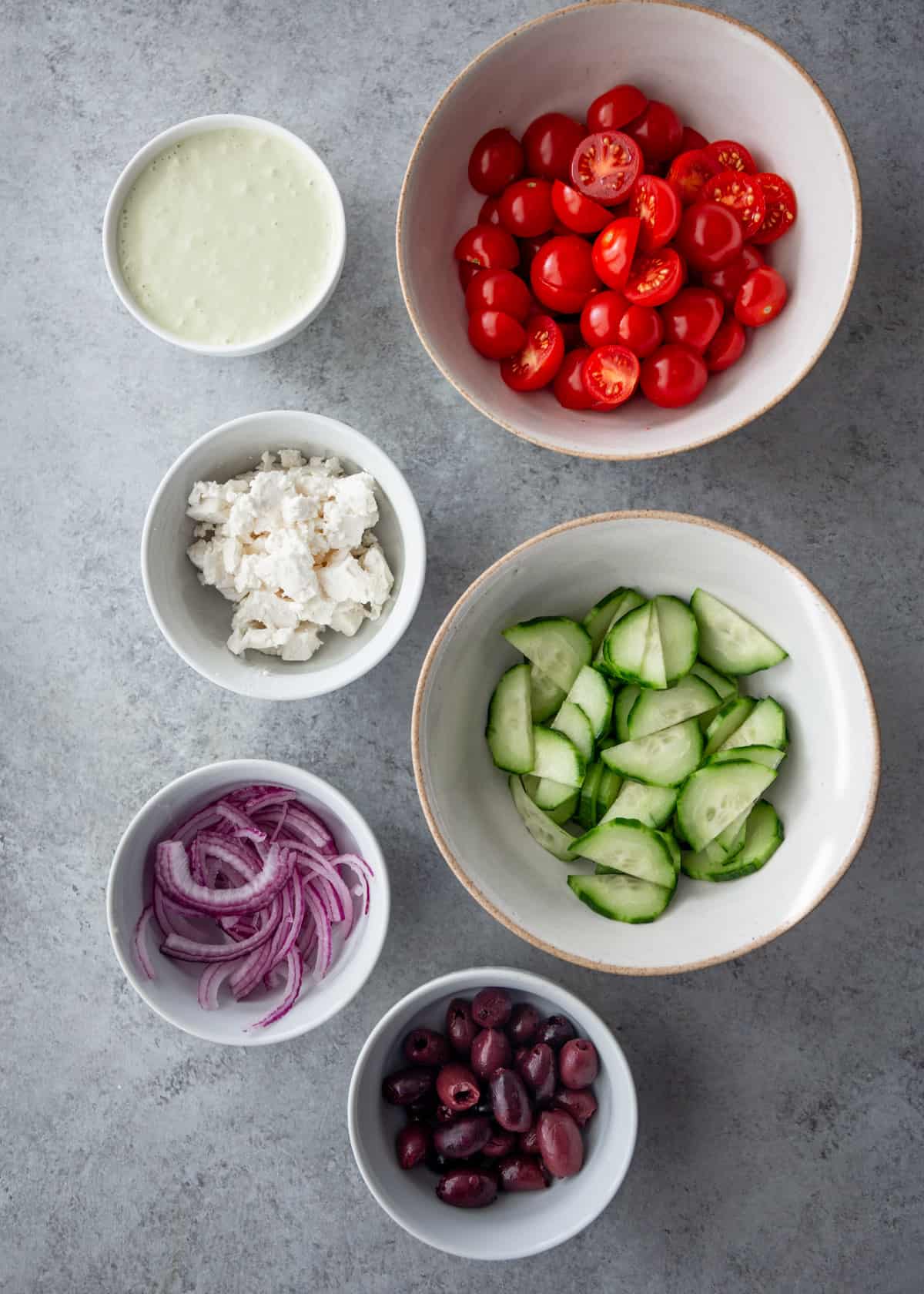 overhead image of ingredients for salad in white bowls on a grey countertop