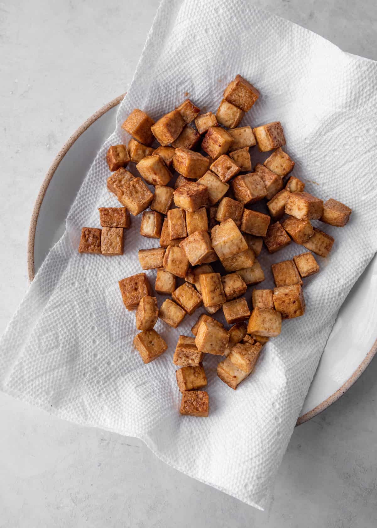 cooked tofu cubes on a white paper towel lined plate