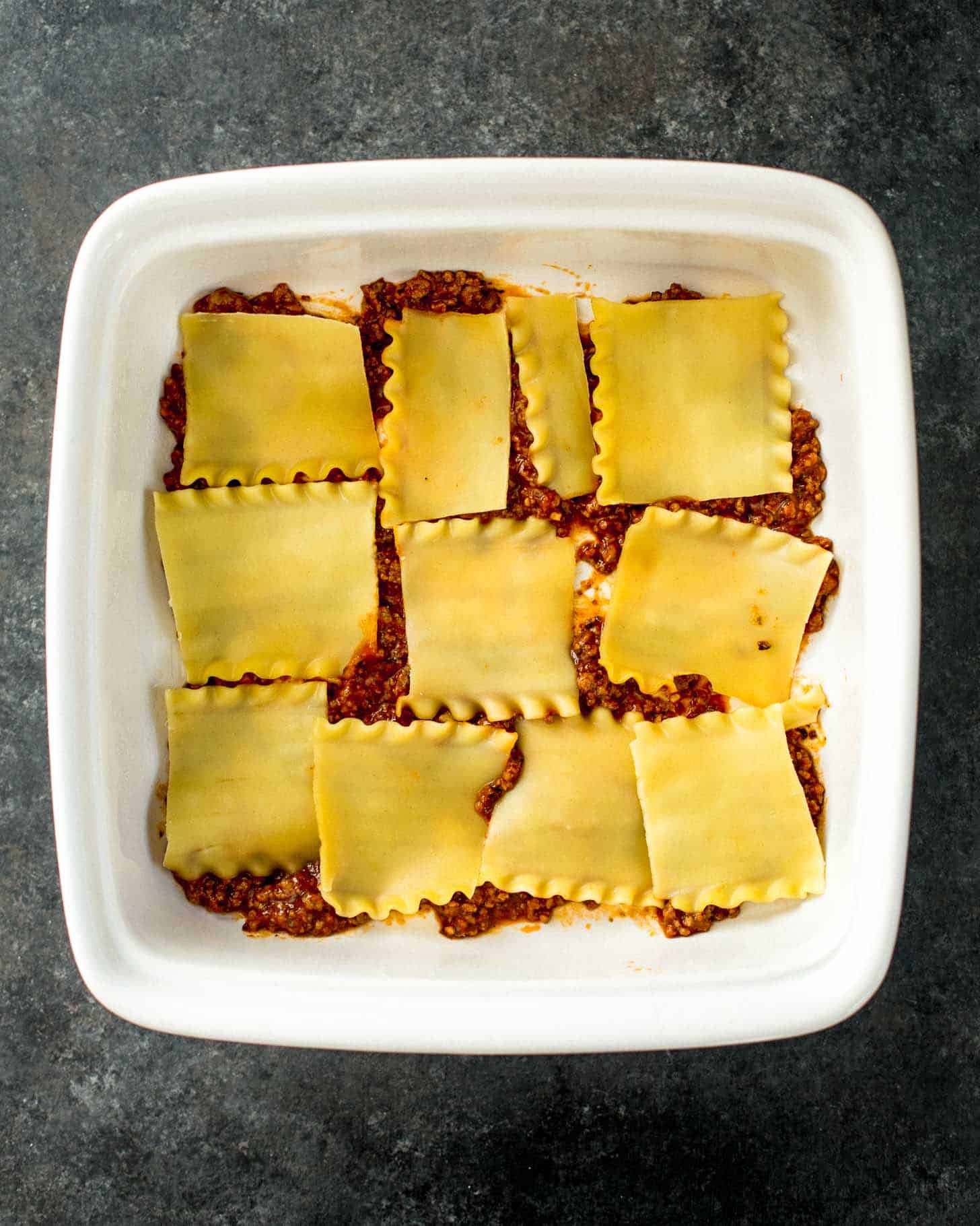 bottom layer of lasagna in a white baking dish