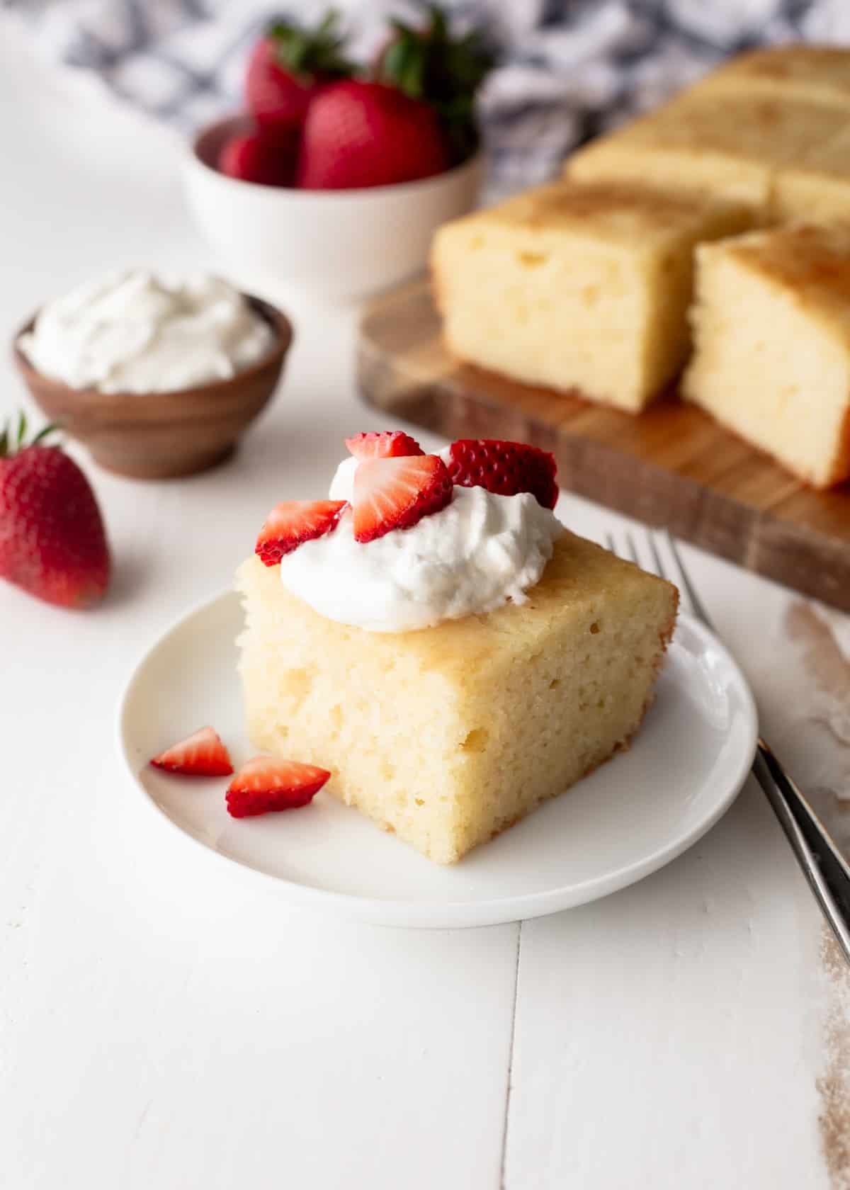 a piece of semolina cake topped with cream and strawberry slices on a small white plate