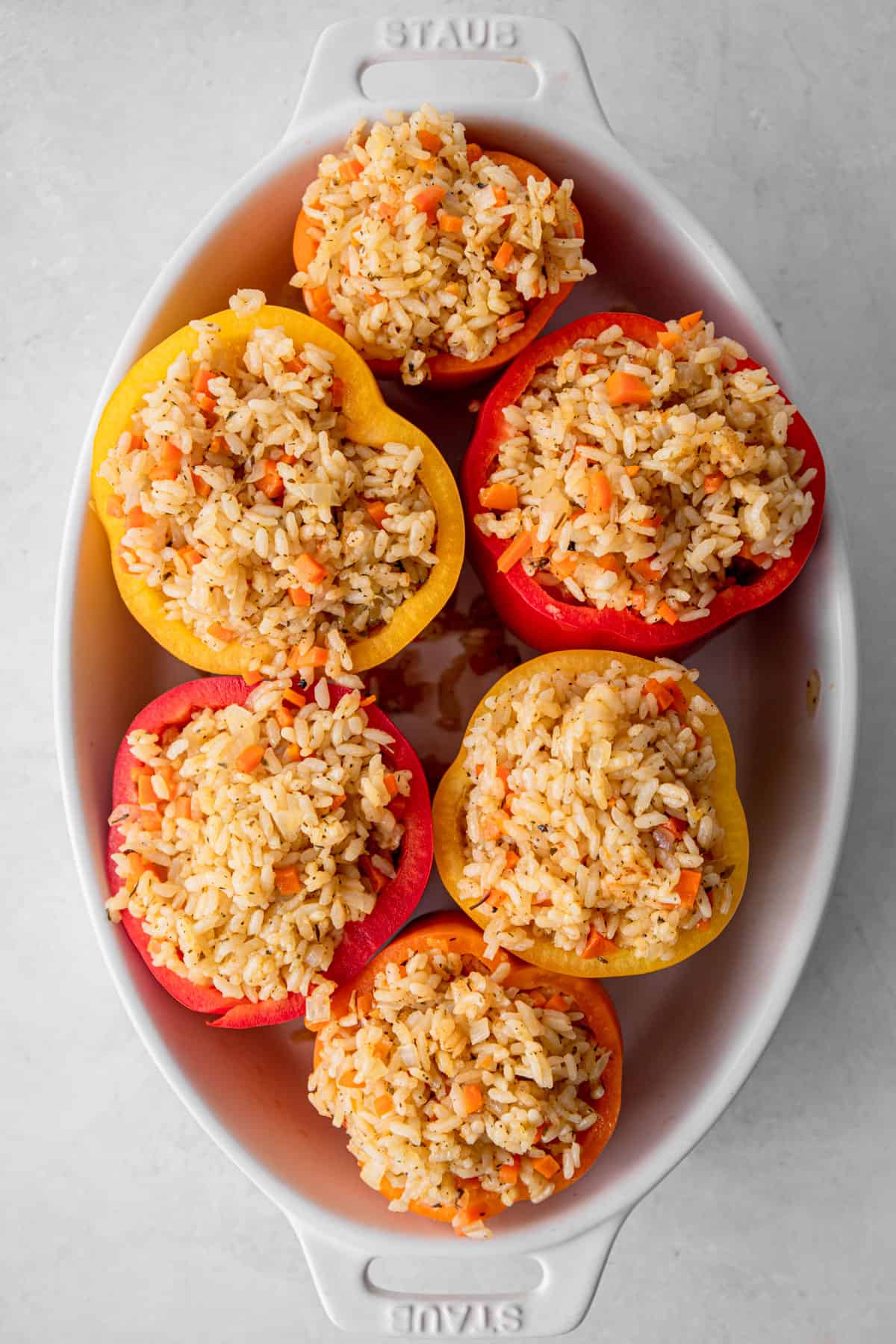 raw stuffed peppers in a white oval baking dish
