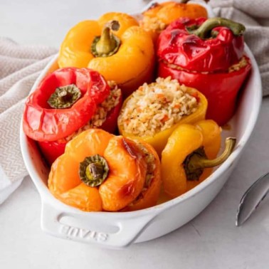 rice and vegetable stuffed peppers in a white baking dish