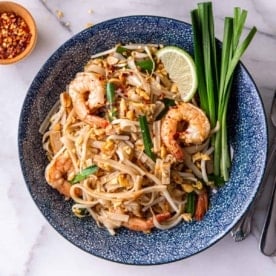square image of Thai noodles with tail-on shrimp in a blue floral bowl