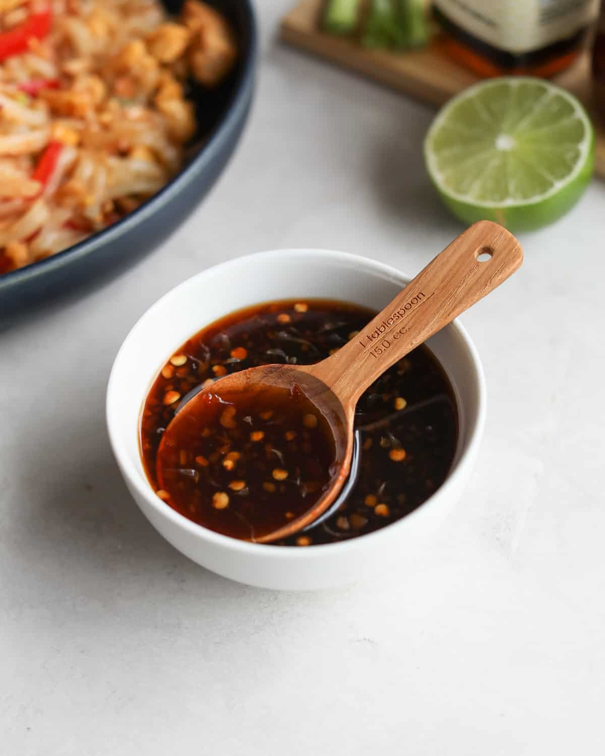 pad thai sauce in a white bowl with a wooden measuring spoon