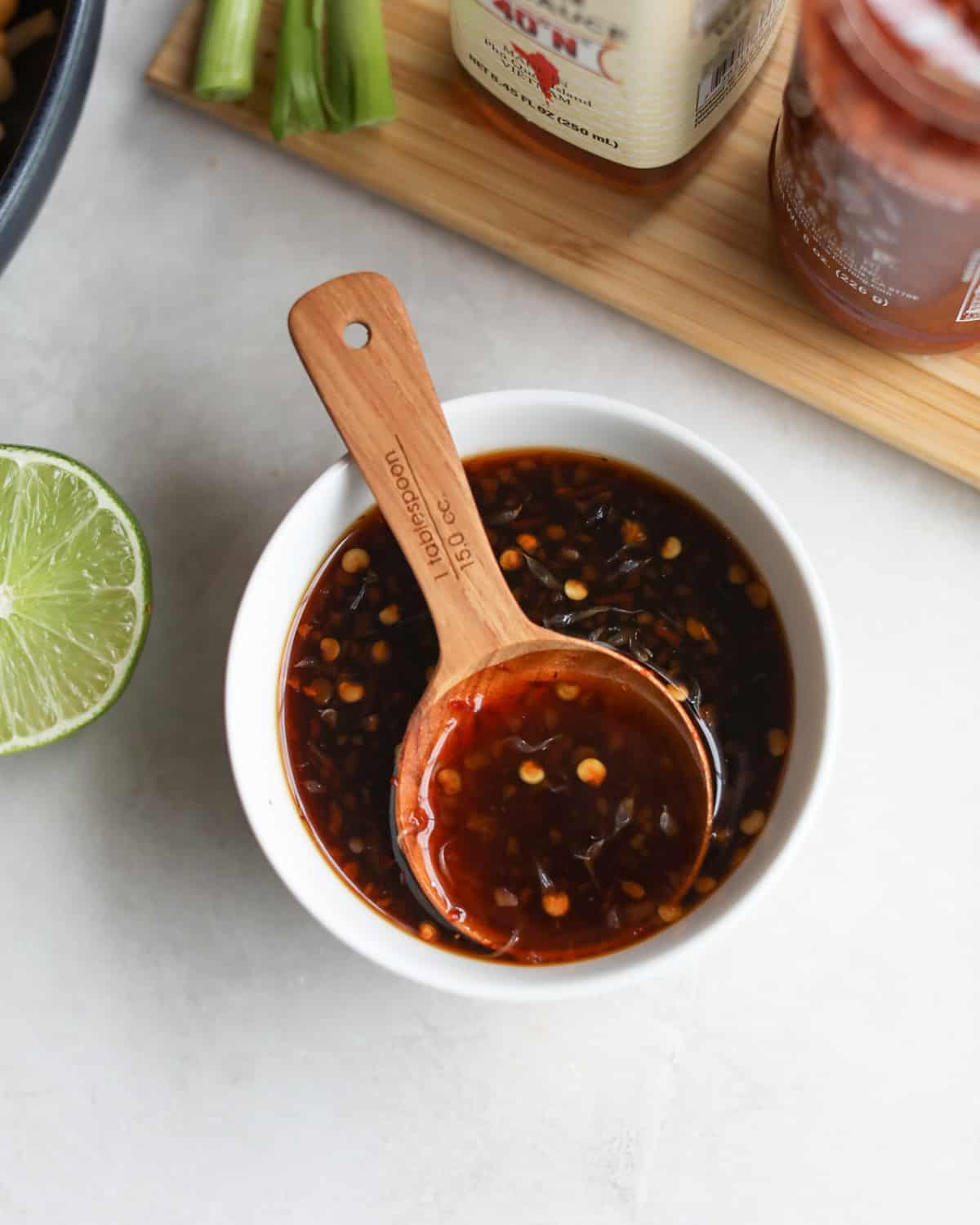 sauce in a small white bowl with a 1 tablespoon wooden measuring spoon