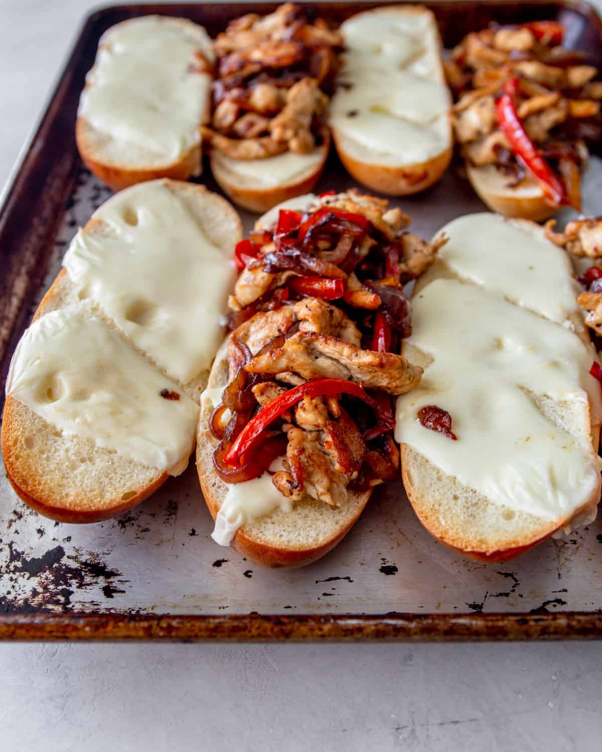 chicken philly sandwiches lying open faced on a sheet pan